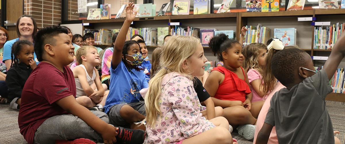 Students listen in the library while some raise their hands